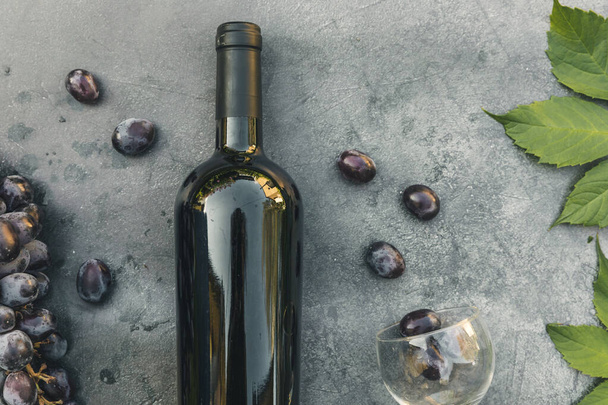 Bottle of red wine, green vine, wineglass and ripe grape on vintage dark stone table background. Top view copy space for text. Wine shop wine bar winery or wine tasting concept. - Photo, Image