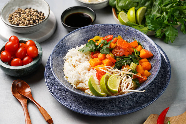 Modrá mísa s červeným thajským zeleninovým kari a rýží Basmati, čerstvým limetem, koriandrem, špenátem, chilli papričkami a cherry rajčaty - Fotografie, Obrázek