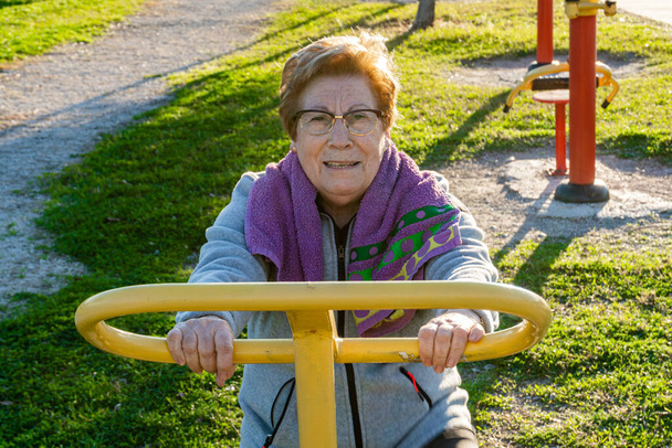 Donna anziana pratica sport sulla cyclette in un parco bio-sano, al tramonto. - Foto, immagini