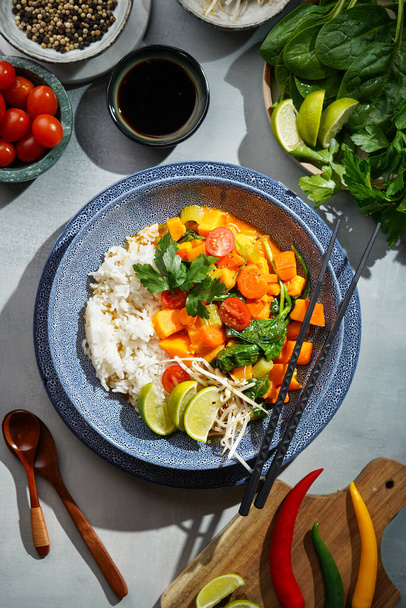 Modrá mísa s červeným thajským zeleninovým kari a rýží Basmati, čerstvým vápnem, koriandrem, špenátem, chilli papričkami a cherry rajčaty, pohled shora - Fotografie, Obrázek