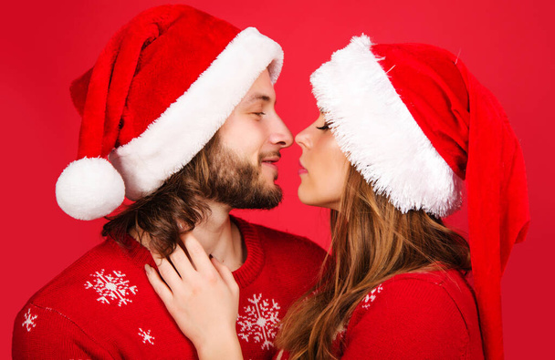 Πρωτοχρονιάτικο ζευγάρι με Χριστουγεννιάτικο καπέλο αγκαλιάζει και φιλάει. Ρομαντικές σχέσεις. Έννοια αγάπης. - Φωτογραφία, εικόνα