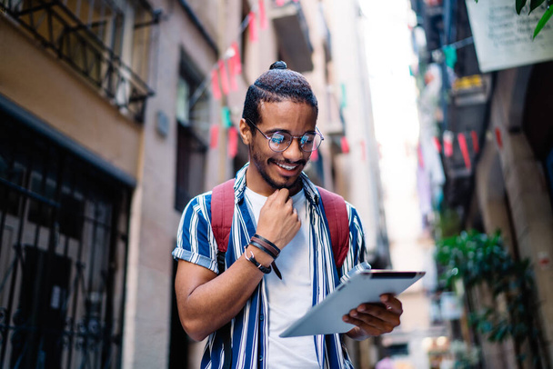 Cheerful african american hipster guy reading message on digital tablet searching information about direction for navigate in city, smiling dark skinned male blogger share content in social networks - Foto, Bild