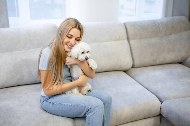 Νεαρή γυναίκα χαλαρώνει και παίζει με το σκύλο (λευκό μαλτέζικο) στο σπίτι. Pet Lover έννοια - Φωτογραφία, εικόνα