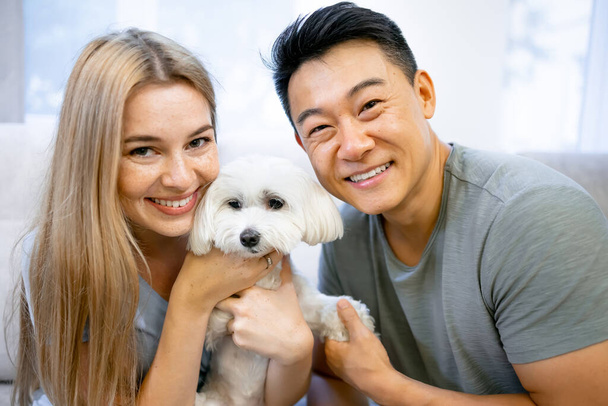 Happy married couple, young girl and cute asian kid spend time sitting with their beloved dog in the cozy room of their country house - Foto, immagini