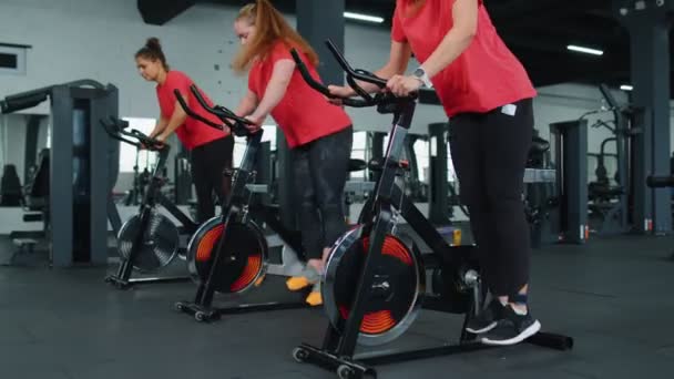 Grupo de mujeres atléticas montando en bicicleta estacionaria de spinning rutina de entrenamiento en el gimnasio, pérdida de peso en interiores - Imágenes, Vídeo