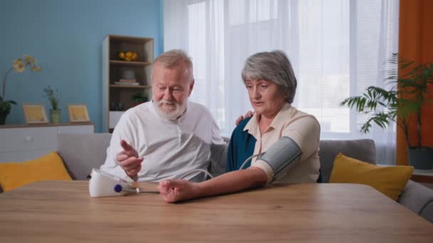 szczęśliwy emeryci dbać o swoje zdrowie, kochający mąż mierzy ciśnienie krwi z tonometrem do starej żony w domu - Materiał filmowy, wideo
