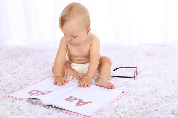 Cute baby boy with book on carpet in room - Foto, imagen