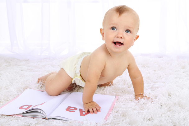 Cute baby boy with book on carpet in room - Fotografie, Obrázek