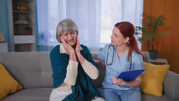 paciente de edad avanzada habla de dolores en la cabeza para asistir al médico, médico femenino en uniforme azul con un estetoscopio apoya a la abuela en casa - Imágenes, Vídeo
