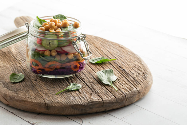 Een pot verse salade op een rustieke houten plank, van achteren verlicht. - Foto, afbeelding