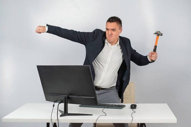 The man gets angry and smashes the monitor with a hammer. An office worker in a rage breaks the computer.  - 写真・画像