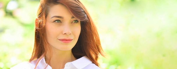 Portret pięknej rudej dziewczyny. Atrakcyjna młoda kobieta ciesząca się czasem spędzonym w parku na wiosennym tle. Baner wiosenny design, reklama nagłówka strony. - Zdjęcie, obraz