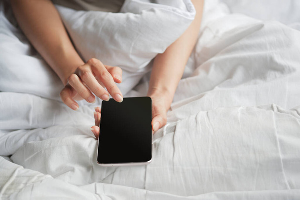 Woman's hand using blank screen smartphone on white bed. Clipping path. - Foto, Imagem