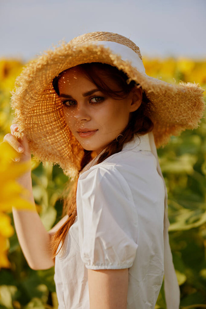 hermosa dulce chica en un sombrero de paja en un vestido blanco un campo de girasoles agricultura paisaje - Foto, imagen