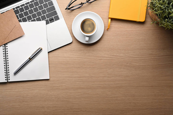 Jednoduchý pracovní prostor s notebookem, šálkem kávy, notebookem a pokojovou rostlinou na dřevěném stole. - Fotografie, Obrázek