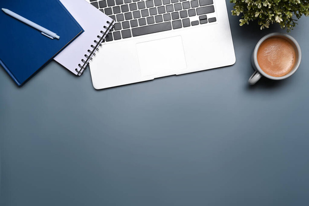 Widok nad głową laptop, roślina doniczkowa, notebook i filiżanka kawy na niebieskim tle. - Zdjęcie, obraz