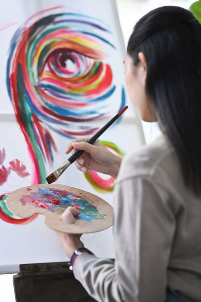Achteraanzicht van vrouwelijke kunstenaar schilderen met aquarel op doek. - Foto, afbeelding