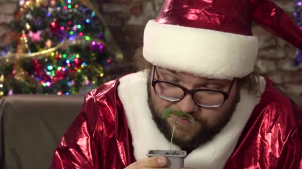 Un jeune homme déguisé en Père Noël tient un petit germe de marijuana dans ses mains et grimaces.4k - Séquence, vidéo