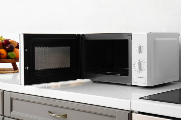 Open microwave oven on counter near light wall - Foto, Bild