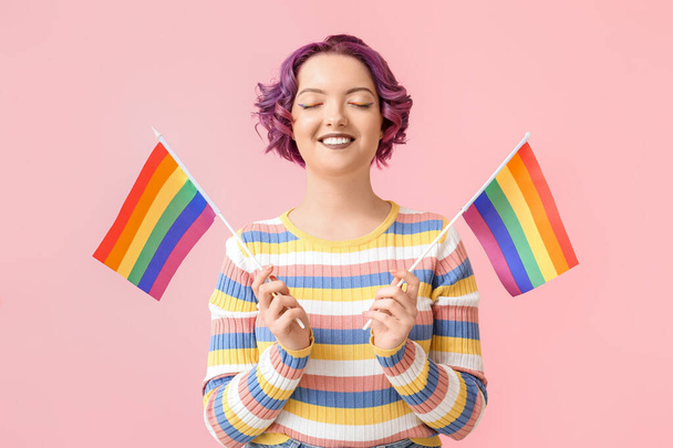 Νεαρή γυναίκα με LGBT σημαίες σε ροζ φόντο - Φωτογραφία, εικόνα