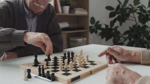 Gros plan de deux hommes âgés jouant aux échecs à table dans une maison de retraite lorsque l'infirmière leur apporte des pilules dans des tasses jetables - Séquence, vidéo