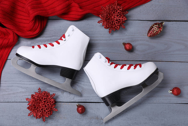 Pair of ice skates, Christmas decor and red scarf on grey wooden background, flat lay - Фото, изображение