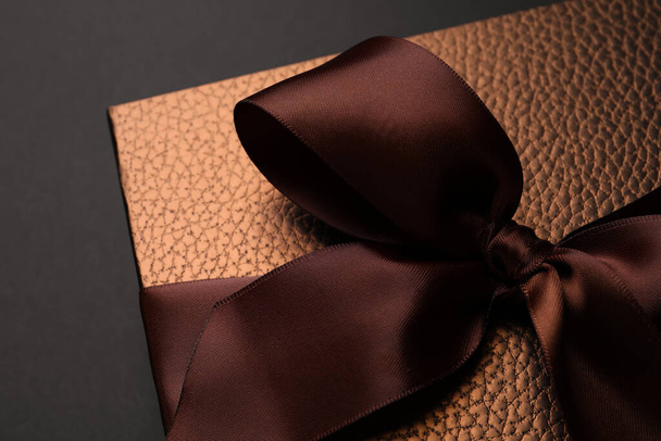 Brown gift box decorated with satin bow on black background, closeup - Photo, Image