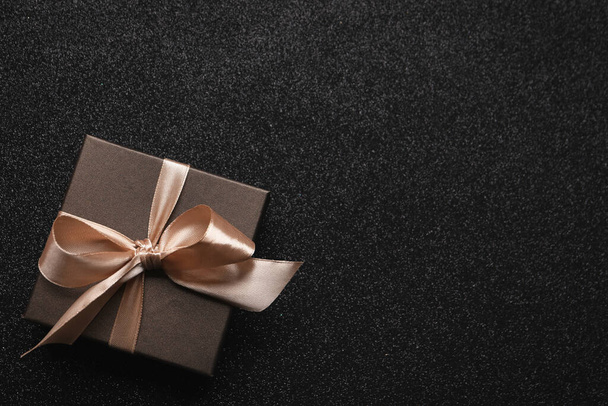 Gift box with golden bow on black background, top view. Space for text - Photo, image