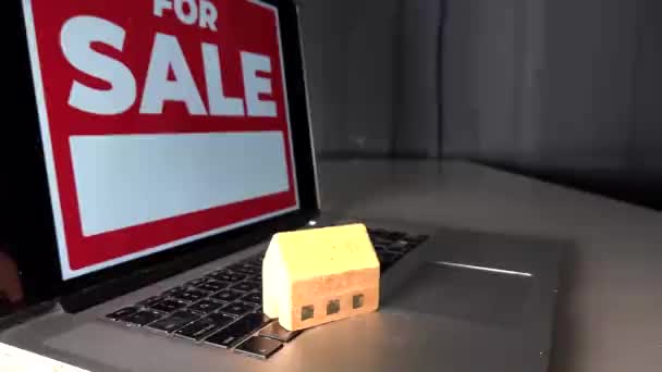 Un letrero de "en venta" en una computadora y una casa de juguetes en un teclado de computadora.  - Metraje, vídeo