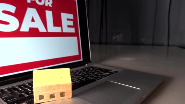 Un letrero de "en venta" en una computadora y una casa de juguetes en un teclado de computadora.  - Metraje, vídeo