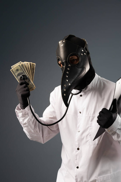 a corrupt doctor in a bathrobe and a plague doctor mask with a wad of money in his hands - Photo, Image