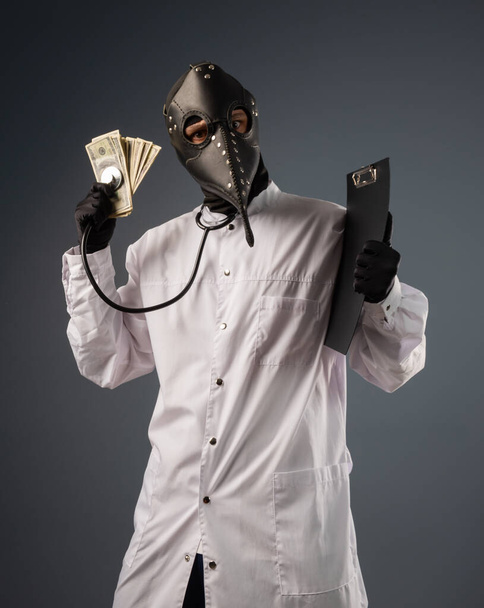 a corrupt doctor in a bathrobe and a plague doctor mask with a wad of money in his hands - Foto, afbeelding