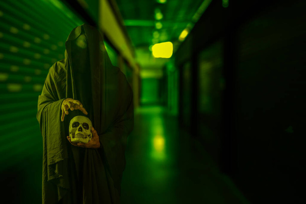 Жахлива сцена страшного чорного чоловіка, який тримає череп в руці в моторошному старому будівельному коридорі
 - Фото, зображення