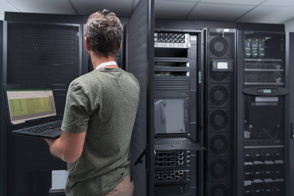 Data Center Engineer Using Laptop Computer. Server Room Specialist Facility with Male System Administrator Working with Data Protection Network for Cyber Security or Cryptocurrency Mining Farm.  - 写真・画像