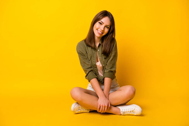 Foto de menina sentar chão pernas cruzadas olhar câmera desgaste verde camisa mini-saia tênis isolado cor amarela fundo. - Foto, Imagem
