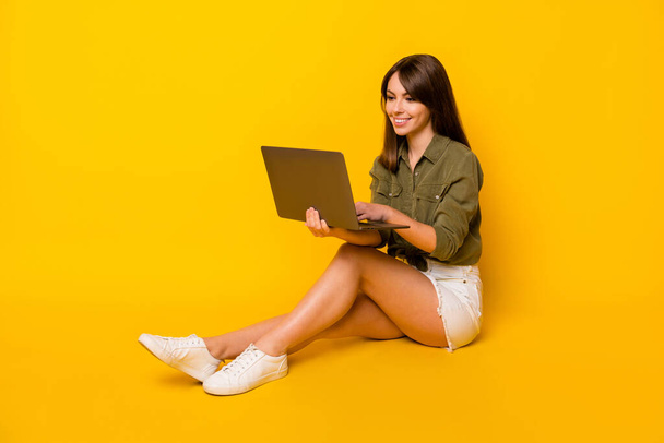 Photo of lady sit floor hold netbook look screen wear green shirt mini skirt sneakers isolated yellow color background. - Фото, зображення