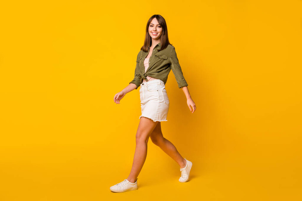 Photo of pretty young girl walk look camera wear green shirt short skirt sneakers isolated yellow color background. - Foto, Imagem