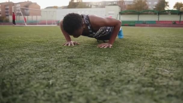 Mladá černošky dívka trénink ve městě stadionu a dělá tlačit nahoru na umělé trávníku fotbalového hřiště - Záběry, video
