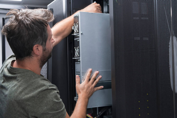 IT engineer working In the server room or data center. The technician puts in a rack a new server of corporate business mainframe supercomputer or cryptocurrency mining farm.  - Photo, Image