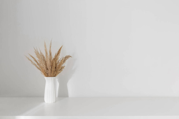 dried wild flowers in white vase on wooden shelf on background white wall - Foto, Imagen