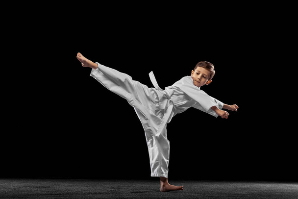 Dynamic portrait of little boy, young karate training alone isolated over white background. Concept of sport, education, skills - Photo, Image