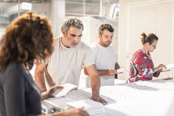 Large group of people, logistic technician workers, female and male, work together on finishing products on the production line in factory and digital printshop office - Foto, afbeelding