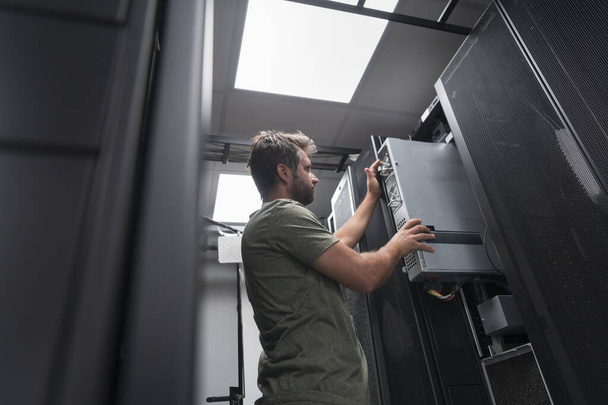 IT engineer working In the server room or data center. The technician puts in a rack a new server of corporate business mainframe supercomputer or cryptocurrency mining farm.  - Foto, afbeelding
