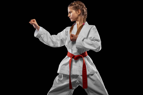 One young girl, teen, taekwondo athlete posing isolated over dark background. Concept of sport, education, skills - Foto, Imagen
