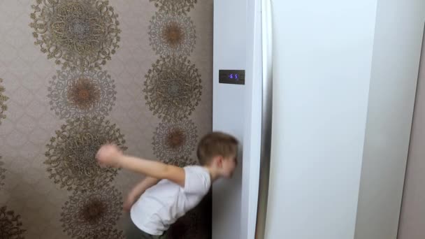 Een kleine jongen opent de koelkast in de keuken en kiest voor een lange tijd producten - Video