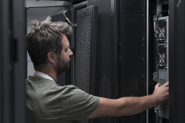IT engineer working In the server room or data center. The technician puts in a rack a new server of corporate business mainframe supercomputer or cryptocurrency mining farm.  - Photo, image