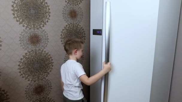 Ein kleiner Junge öffnet den Kühlschrank in der Küche und sucht sich lange Produkte aus - Filmmaterial, Video