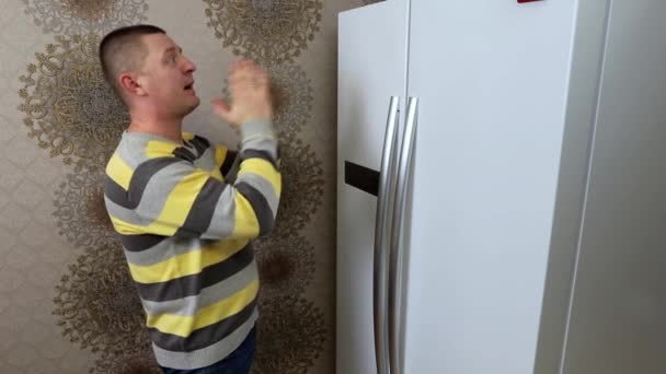 Egy férfi imádkozik a hűtő előtt, hogy legyen benne finom étel. - Felvétel, videó