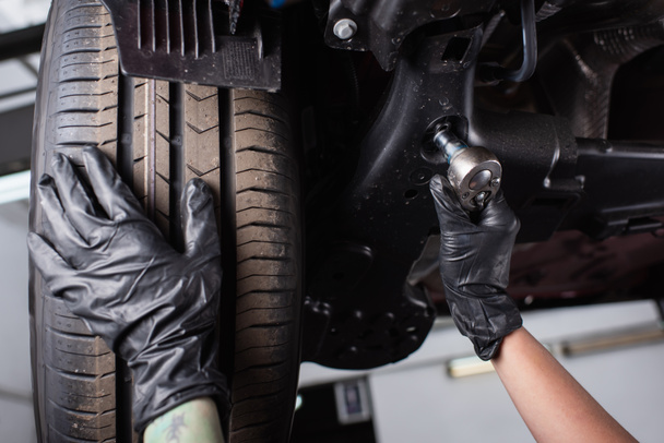 Widok mechanika w rękawiczkach z kluczem w pobliżu koła samochodu w garażu  - Zdjęcie, obraz