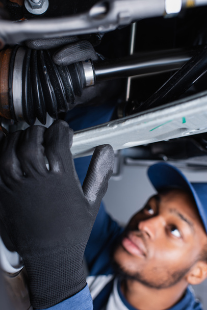 Wazig Afrikaans-Amerikaanse monteur in handschoenen werken met auto in de garage  - Foto, afbeelding